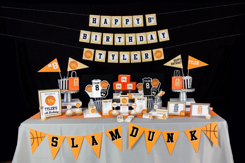 May include: A basketball-themed birthday party table setting with orange and black decorations. The table is covered in a gray tablecloth with a banner that reads "SLAM DUNK". There are several decorations, including a basketball-shaped cake, a basketball-shaped pi&ntilde;ata, and a basketball-shaped balloon. The table is also decorated with orange and black streamers and balloons.
