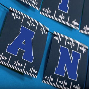 Puede incluir: Una pancarta azul y blanca con las letras "AND" en ella. Las letras est&aacute;n en una fuente en negrita, de bloque y est&aacute;n delineadas en blanco. La pancarta est&aacute; hecha de un material azul oscuro y tiene una regla impresa en ella.
