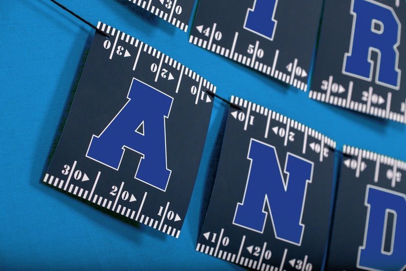 Puede incluir: Una pancarta azul y blanca con las letras "AND" en ella. Las letras est&aacute;n en una fuente en negrita, de bloque y est&aacute;n delineadas en blanco. La pancarta est&aacute; hecha de un material azul oscuro y tiene una regla impresa en ella.