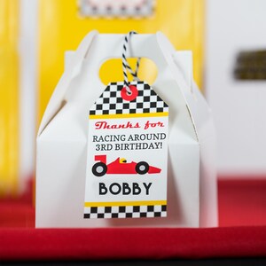 May include: White favor box with a black and white checkered tag. The tag has a red race car with the text "Thanks for racing around 3rd birthday! BOBBY".