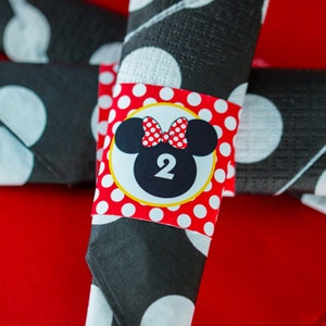 Könnte beinhalten: Rote und schwarze Tupfen-Serviettenringe mit einem Minnie Mouse-Motiv. Der Ring zeigt einen gelben Kreis mit einem Schwarzweißbild von Minnie Mouse mit einer roten Schleife und der Zahl 2.