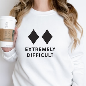 May include: White sweatshirt with two black diamond symbols and the text "EXTREMELY DIFFICULT" printed on the front.