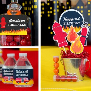 May include: Firefighter themed birthday party decorations with red and yellow fire truck and fire hydrant designs. The decorations include a cake topper with the text "Happy 3rd Birthday", a jar of candy with the text "Five Alarm Fireballs", and water bottles with personalized labels.