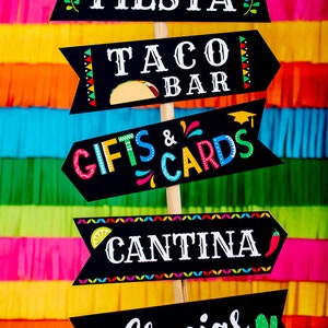 Op de afbeelding: Vijf zwarte pijl-vormige borden van schoolbord met kleurrijke versieringen en tekst. De borden tonen "Let's Fiesta", "Taco Bar", "Gifts & Cards", "Cantina" en "Gracias".