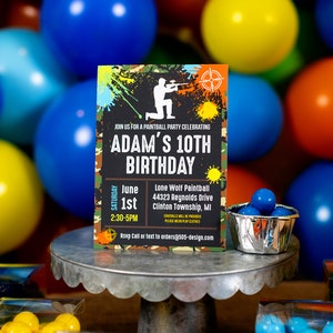 May include: A green, black, and orange birthday party invitation with a silhouette of a person holding a paintball gun. The invitation says "Join us for a paintball party celebrating Adam's 10th Birthday" and includes the date, time, and location of the party.