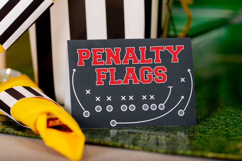 May include: A black sign with white text that reads "PENALTY FLAGS" in red letters. The sign has a football field diagram with white lines and circles.