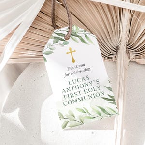 Puede incluir: Etiqueta de favor blanca con follaje verde y una cruz dorada. El texto dice "Gracias por celebrar la Primera Comuni&oacute;n de Lucas Anthony."