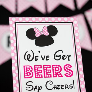 May include: Pink and white polka dot sign with a black and white image of Minnie Mouse. The sign says "We've got beers Say Cheers!"