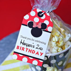 May include: Red and white polka dot favor bag with a black and white Minnie Mouse head with a red bow. The bag contains popcorn and has a tag that says "Thank you for celebrating Harper's 2nd Birthday."