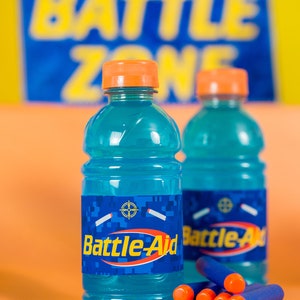May include: Two blue plastic bottles with orange caps and labels that say "Battle-Aid" on a orange surface with blue and orange dart-like objects.