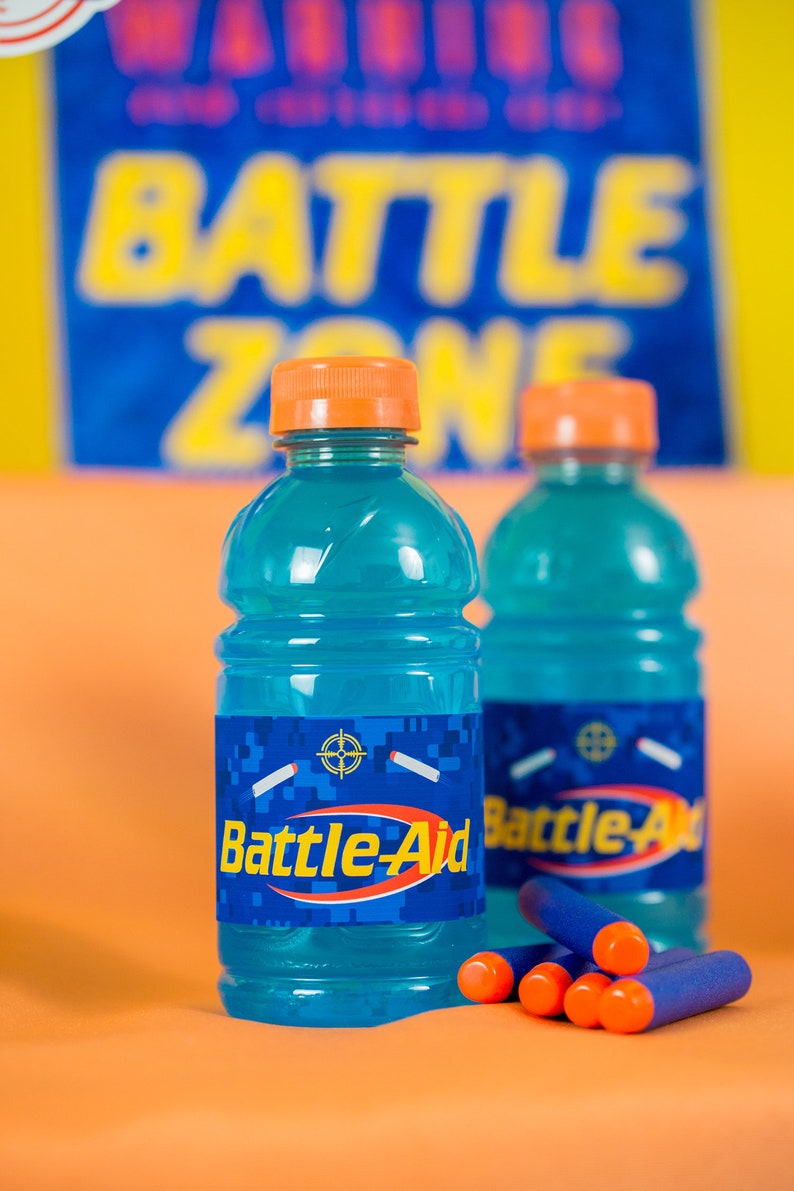 May include: Two blue plastic bottles with orange caps and labels that say "Battle-Aid" on a orange surface with blue and orange dart-like objects.