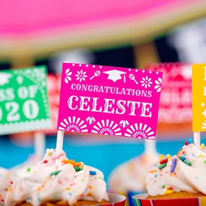 Op de afbeelding: Een close-up van cupcakes die versierd zijn met kleurrijke sprinkles en bedekt zijn met kleine vlaggetjes. De vlaggetjes zijn versierd met een afstudeerhoed en de tekst "Class of 2020", "Congratulations Celeste" en "Rome High School".
