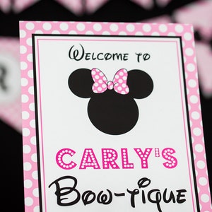 May include: Pink and white polka dot sign with black text that says "Welcome to Carly's Bow-tique" with a black and white silhouette of Minnie Mouse with a pink polka dot bow.