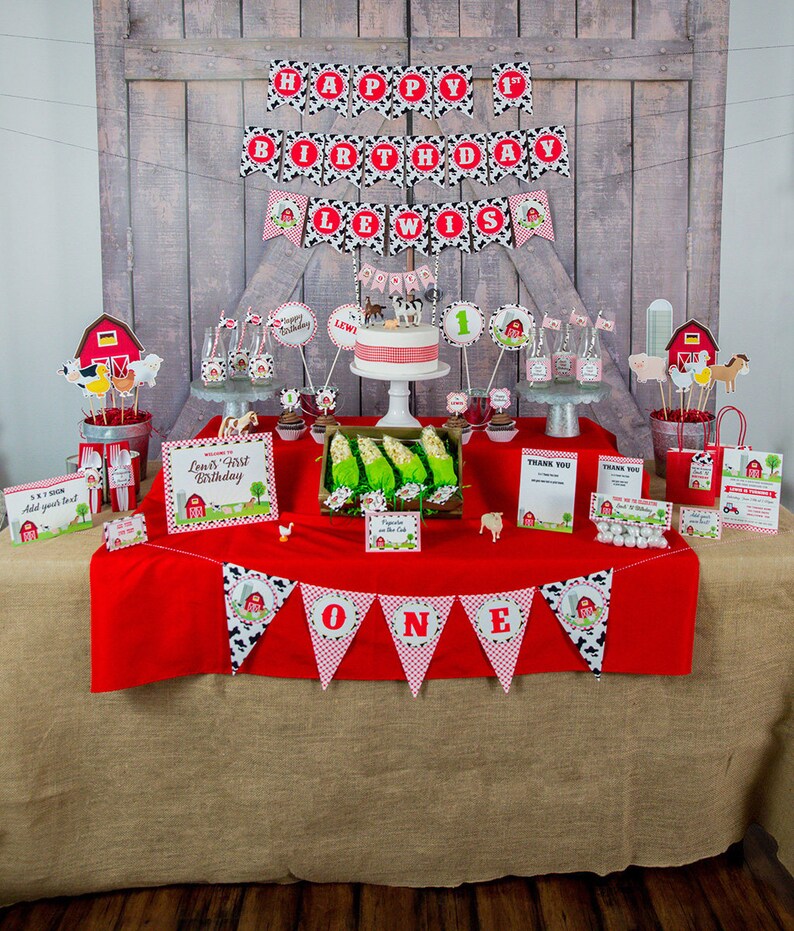May include: A red and white tablecloth with a banner that says "ONE" in black and white letters. The table is decorated with a farm-themed birthday party decorations, including a cake, cupcakes, and a banner that says "Happy 1st Birthday Lewis".