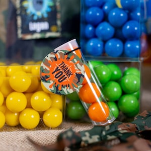 May include: A clear plastic tube filled with orange and green candy. A round tag with a camouflage pattern and the words "Thank You" in orange letters is attached to the tube.