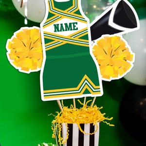 May include: Green and gold cheerleader outfit cutout with the word "NAME" on the front, two yellow pom-poms, a black megaphone, and a black and white striped box filled with yellow shredded paper.