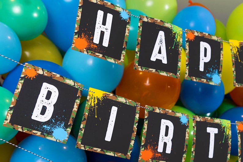 May include: A black and green camouflage banner with white letters spelling "Happy Birthday". The banner is decorated with colorful paint splatters.