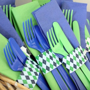 May include: A close-up of green and blue plastic forks and knives wrapped in green, black, and white patterned paper napkins. The napkins are tied with a ribbon.