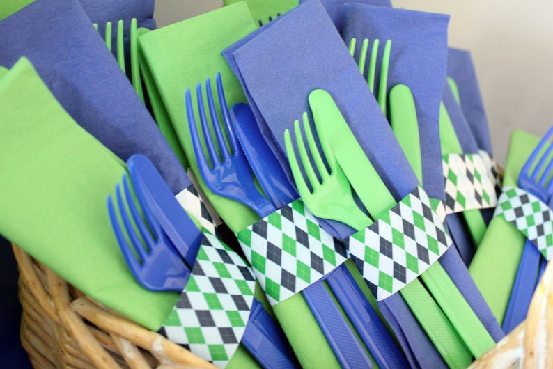 May include: A close-up of green and blue plastic forks and knives wrapped in green, black, and white patterned paper napkins. The napkins are tied with a ribbon.