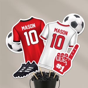 May include: A collection of soccer-themed cutouts, including two jerseys with "MASON 10" on the back, a soccer ball, a foam finger with "#1", and a pair of black soccer cleats. The jerseys are red and white.
