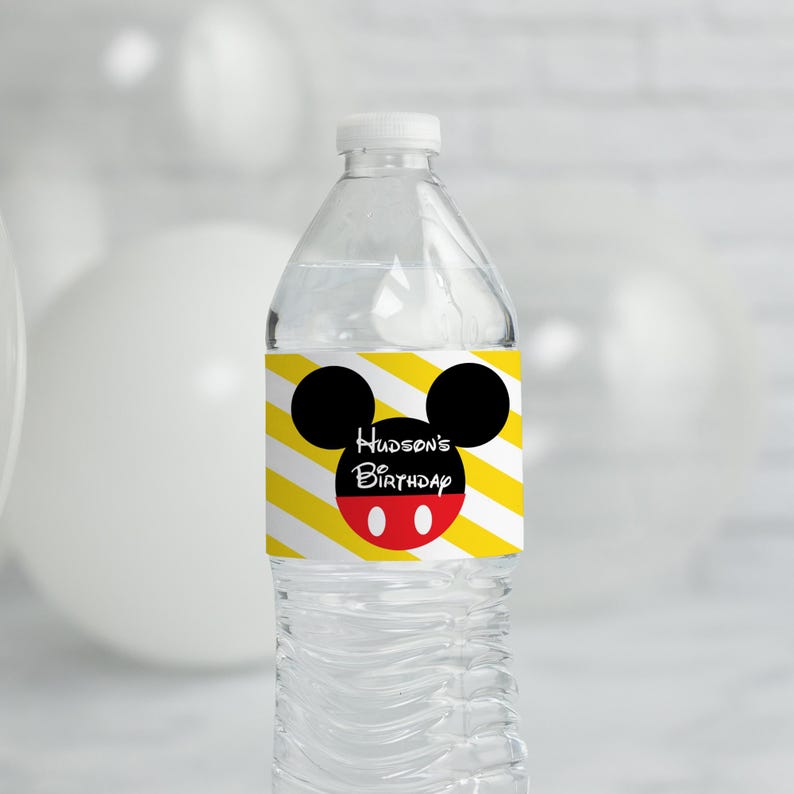May include: A clear plastic water bottle with a yellow and white striped label featuring a black Mickey Mouse head with red circles. The label says "Hudson's 1st Birthday".