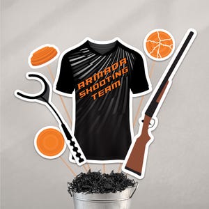 May include: A collection of cut-out images related to the Armada Shooting Team. Includes a black and orange short-sleeve shirt with the team name, a shotgun, orange clay targets, and a clay target thrower. The items are arranged in a decorative display.