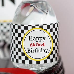 May include: A clear plastic water bottle with a black and white checkered label that says "Happy third Birthday".