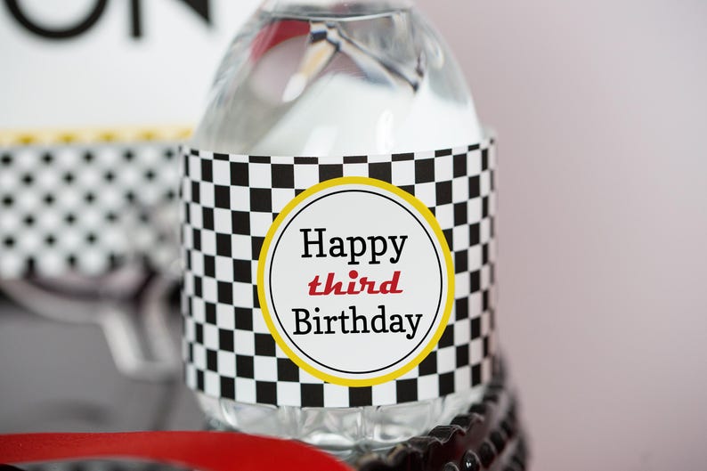 May include: A clear plastic water bottle with a black and white checkered label that says "Happy third Birthday".