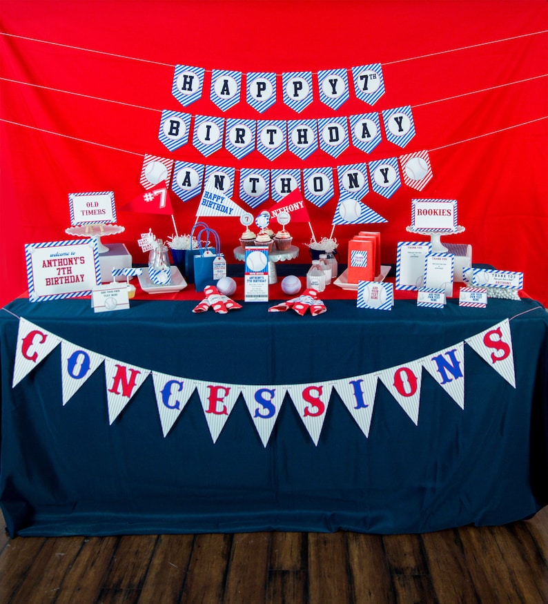 May include: A baseball-themed birthday party setup with a red backdrop and a navy blue table. Decorations include pennant banners that read "Happy 7th Birthday Anthony" and "Concessions." The table is adorned with baseball-themed treats and party favors.