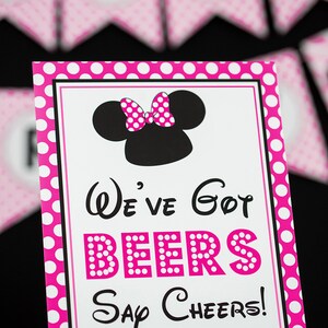 Puede incluir: Un cartel de lunares rosa y blanco con una cabeza de Minnie Mouse negra y un lazo. El cartel dice "We've got beers Say Cheers!"