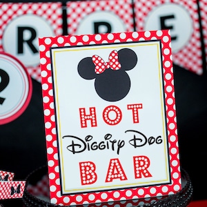 以下が含まれることがあります： ミニーマウスのシルエットとリボンが付いた「Hot Diggity Dog Bar」のサイン。サインは赤い水玉模様のボーダーで、黒いケーキスタンドの上にあります。背景には赤と白の水玉模様のバナーがあります。