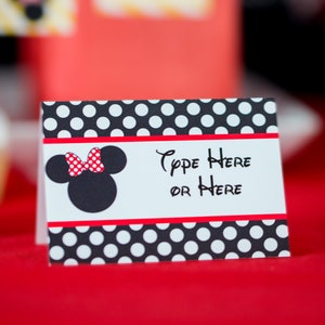 Peut inclure: Une carte &agrave; pois noirs et blancs avec un n&oelig;ud rouge et une silhouette noire de la t&ecirc;te de Mickey Mouse. La carte dit "Type Here or Here".