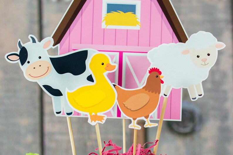 Puede incluir: Un granero rosa con un pajar en la ventana, una vaca blanca, un pato amarillo, una gallina marr&oacute;n y una oveja blanca. Todos los animales est&aacute;n en palos y son parte de un centro de mesa con tem&aacute;tica de granja.