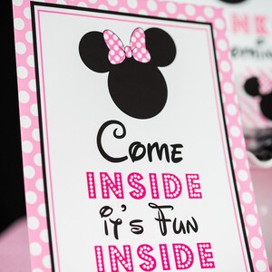 May include: Pink and white polka dot sign with a black and white image of Minnie Mouse. The sign says "Come Inside It's Fun Inside".