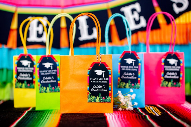 Op de afbeelding: Een set kleurrijke cadeauzakken met etiketten met een afstudeerthema. De etiketten hebben een zwarte krijtbordachtergrond met kleurrijke strepen en een afstudeerpet. De tekst op de etiketten luidt "Bedankt voor het vieren van Celeste's afstuderen".