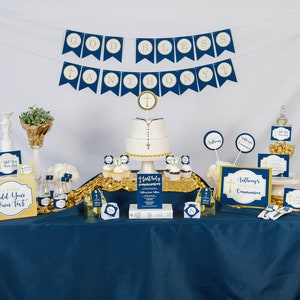 K&ouml;nnte beinhalten: Eine blaue und goldene Tischdekoration f&uuml;r eine Erstkommunionsparty mit einem Kuchen, Cupcakes und Dekorationen. Das Banner lautet "God Bless Anthony".