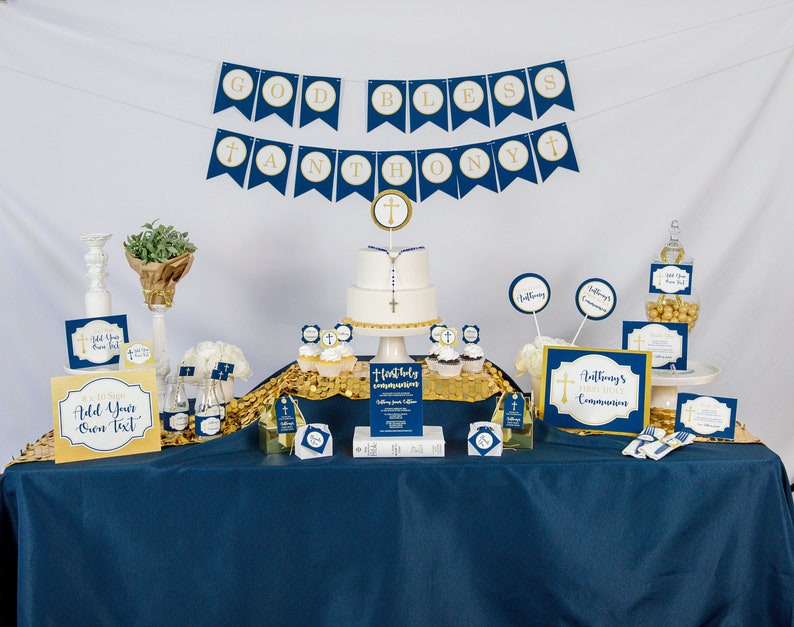 K&ouml;nnte beinhalten: Eine blaue und goldene Tischdekoration f&uuml;r eine Erstkommunionsparty mit einem Kuchen, Cupcakes und Dekorationen. Das Banner lautet "God Bless Anthony".
