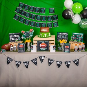 Puede incluir: Una mesa de fiesta con tem&aacute;tica de f&uacute;tbol con decoraciones verdes y negras. La mesa tiene un mantel marr&oacute;n y una pancarta con las palabras "Feliz cumplea&ntilde;os n&uacute;mero 10 Anderson". Hay cupcakes con forma de bal&oacute;n de f&uacute;tbol, un pastel con forma de bal&oacute;n de f&uacute;tbol y un cartel que dice "Stadium Snack".