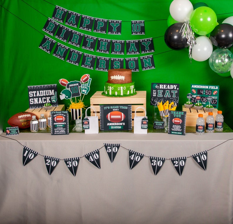 Puede incluir: Una mesa de fiesta con tem&aacute;tica de f&uacute;tbol con decoraciones verdes y negras. La mesa tiene un mantel marr&oacute;n y una pancarta con las palabras "Feliz cumplea&ntilde;os n&uacute;mero 10 Anderson". Hay cupcakes con forma de bal&oacute;n de f&uacute;tbol, un pastel con forma de bal&oacute;n de f&uacute;tbol y un cartel que dice "Stadium Snack".