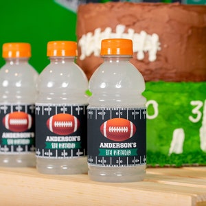 Puede incluir: Tres botellas de pl&aacute;stico transparentes con tapas naranjas y etiquetas en blanco y negro. Las etiquetas muestran un gr&aacute;fico de f&uacute;tbol y el texto "Anderson's 5th Birthday".