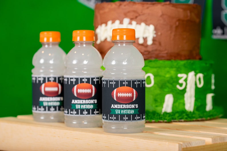Puede incluir: Tres botellas de pl&aacute;stico transparentes con tapas naranjas y etiquetas en blanco y negro. Las etiquetas muestran un gr&aacute;fico de f&uacute;tbol y el texto "Anderson's 5th Birthday".