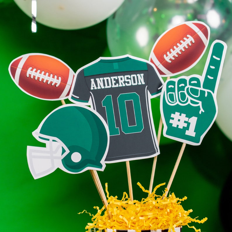 May include: Green, white and black football-themed party decorations. The decorations include a football jersey with the name "Anderson" and the number "10", a football helmet, a football and a foam finger with the number "1".
