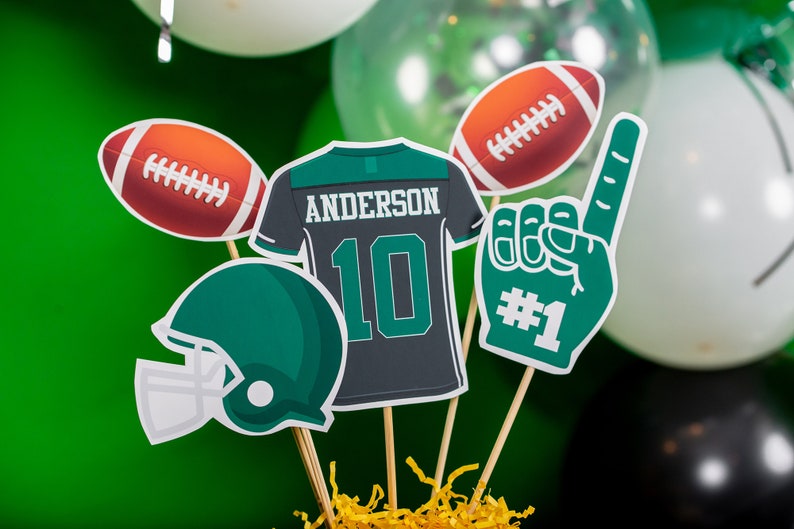 May include: A football-themed centrepiece with a green and white football helmet, a green and white foam finger with the number "#1", a green and white football, a green and white jersey with the name "ANDERSON" and the number "10", and a brown and white football.