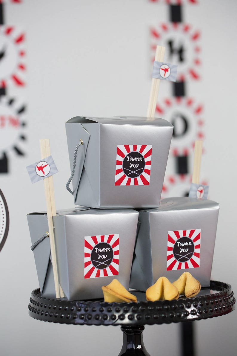 May include: Three silver take-out containers with red and white striped stickers that say "Thank You" with chopsticks and fortune cookies on a black cake stand.