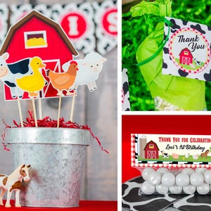 May include: A red barn with a white window and a yellow hay bale inside. There are farm animal cutouts on sticks in front of the barn, including a cow, a duck, a chicken, and a sheep. The cutouts are in a silver metal bucket with red and white shredded paper inside. There is a brown and white toy horse in front of the bucket.