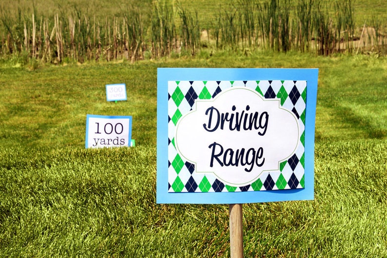May include: A blue sign with a green and black diamond pattern reads "Driving Range". There are two smaller signs in the background that read "100 yards" and "300 yards".