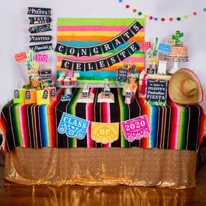 Op de afbeelding: Een afstudeerfeesttafel die is gedecoreerd in een fiesta-thema. De tafel is bedekt met een zwart-rood gestreept tafelkleed met een gouden glittertafelkleed eronder. De tafel is versierd met verschillende items, waaronder een banner met de tekst "Congrats Celeste", een bord met de tekst "Welcome to Celeste's Graduation Fiesta" en een taart met de tekst "Class of 2020".