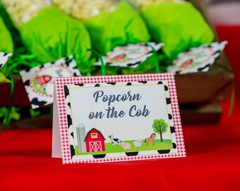 May include: A red and white checkered sign with black polka dots reads "Popcorn on the Cob". The sign features a cartoon farm scene with a red barn, a silo, a cow, a pig, a sheep, and a horse.