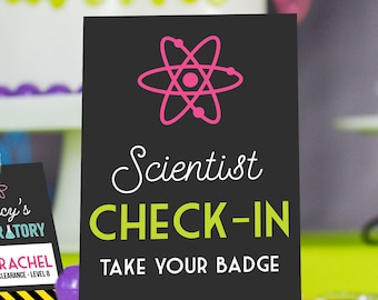 May include: Black sign with a pink atom symbol and white text that reads "Scientist Check-In Take Your Badge".