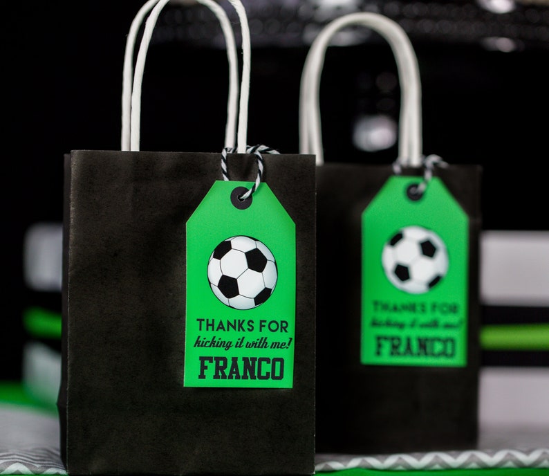 Puede incluir: Dos bolsas de regalo negras con asas blancas y etiquetas verdes. Las etiquetas tienen un gr&aacute;fico de un bal&oacute;n de f&uacute;tbol y el texto "Gracias por patear conmigo! Franco".